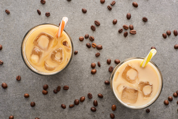 top view of ice coffee with straws and coffee grains on grey background - Foto, Imagem