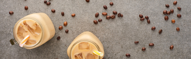 Draufsicht auf frischen Eiskaffee in Glasgläsern mit Strohhalmen und Kaffeekörnern auf grauem Hintergrund, Panoramaaufnahme - Foto, Bild