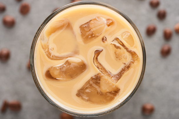 close up view of ice coffee in glass with straw and coffee grains on grey background - Fotó, kép