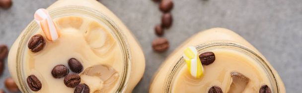 selective focus of ice coffee in glass jar with straw near coffee grains on grey background, panoramic shot - Φωτογραφία, εικόνα