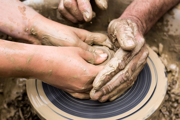 2組の手が陶器の車輪に粘土製品を作る - 写真・画像