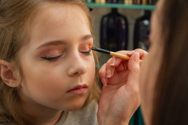 een klein meisje doet make-up voordat hij op het podium presteert. Voorbereiding voor de voorstelling in de kleedkamer - Foto, afbeelding