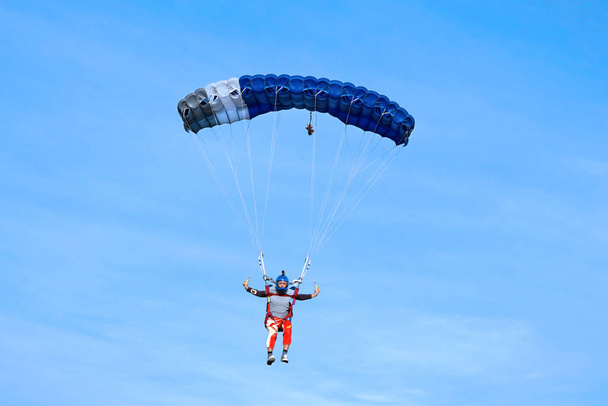 Fallschirmspringer mit dunkelblauem Fallschirm auf dem Hintergrund blauer Himmel - Foto, Bild
