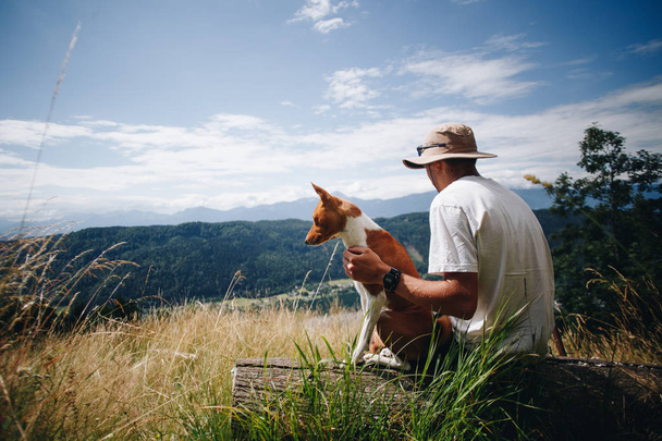Man in hat sits with best friend dog puppy at top - Φωτογραφία, εικόνα