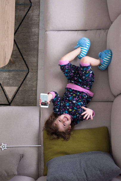 top view of little girl using a smartphone on the sofa - Foto, imagen