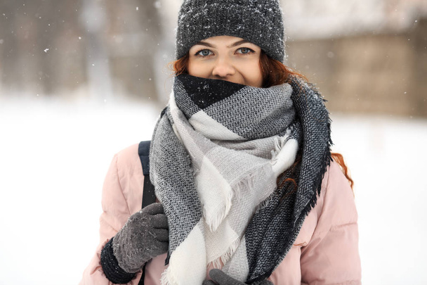 Young cute white caucasian girl in pink down jacket, cap, warm scarf and gloves stands on the street in winter. - Fotografie, Obrázek