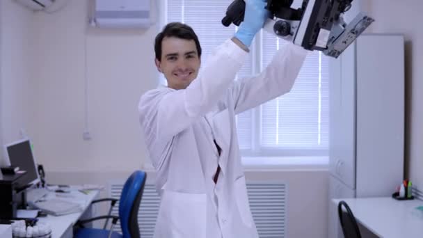 Young man laboratory technician is dancing in lab with microscopes in hands. - Felvétel, videó