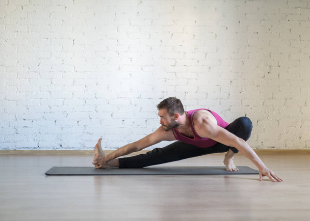 Caucasian man doing stretching, warm-up, yoga on grey mat in fitness studio, loft style, selective focus. - Foto, Bild