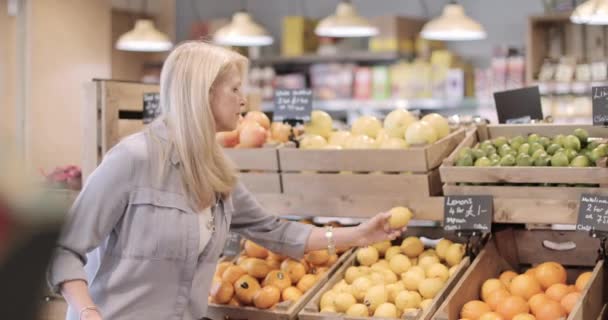 Senior female shopper buying fruit in a grocery store - Filmati, video