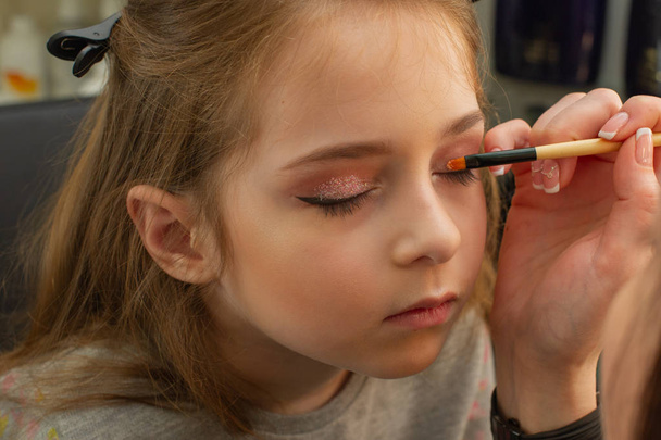a little girl doing makeup before performing on stage. Preparation before the performance in the dressing room - Фото, изображение