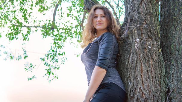 Beautiful woman standing near a tree and looking at the camera - Photo, image