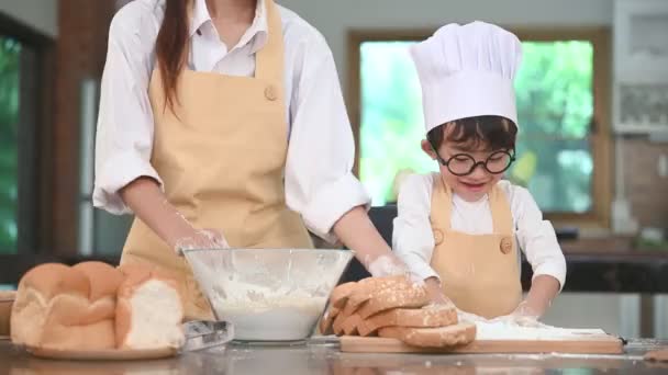 Милый маленький азиатский мальчик и красивая мать просеивает тесто муки в домашней кухне на столе для подготовки к выпечке пекарни и торта. Тайские дети забавно играют с мукой. Концепция семейной жизни
 - Кадры, видео