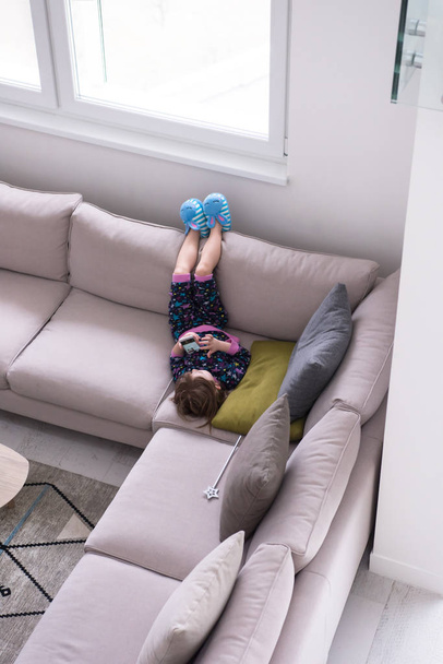 little girl using a smartphone on the sofa at home - Foto, imagen