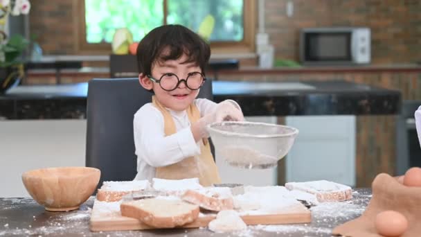 Menino asiático bonito peneirando farinha de massa com peneira peneira escorredor na cozinha em casa para se preparar para assar padaria e bolo. Estilo de vida e Educação das pessoas. Crianças tailandesas brincando com farinha como chef engraçado
 - Filmagem, Vídeo
