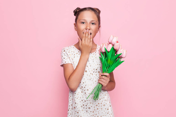 Portrait of a pretty teenage girl, shocked girl covers her mouth with her hand, in a stylish dress with a bouquet of flowers - Fotó, kép