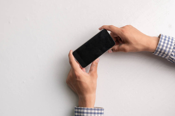 manos sosteniendo vacío teléfono inteligente negro en blanco sobre una superficie blanca, espacios de copia maqueta
 - Foto, Imagen