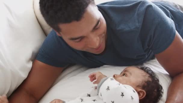 Close of millennial African American father lying on bed playing with his newborn baby son - Filmati, video