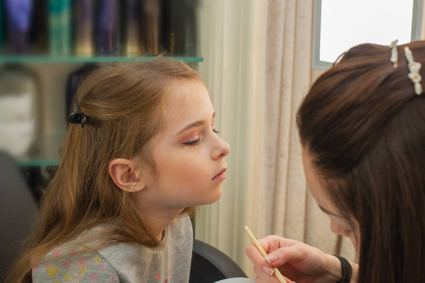 een klein meisje doet make-up voordat hij op het podium presteert. Voorbereiding voor de voorstelling in de kleedkamer - Foto, afbeelding