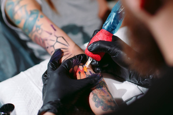 Professional tattoo artist makes a tattoo on a young girls hand. - Foto, afbeelding