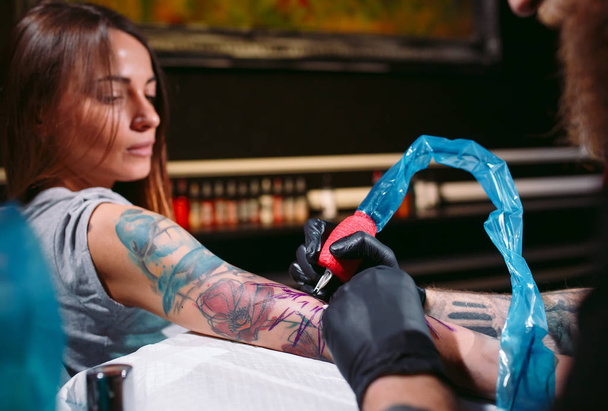 Professional tattoo artist makes a tattoo on a young girls hand. - Zdjęcie, obraz