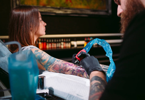 Professional tattoo artist makes a tattoo on a young girls hand. - Фото, изображение