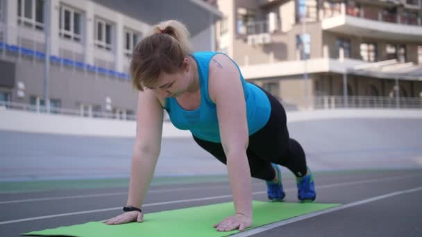 Mujer con sobrepeso haciendo flexiones en el estadio deportivo
 - Metraje, vídeo