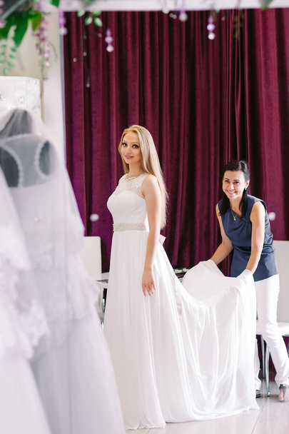 Female trying on wedding dress in a shop with women assistant. - Foto, imagen
