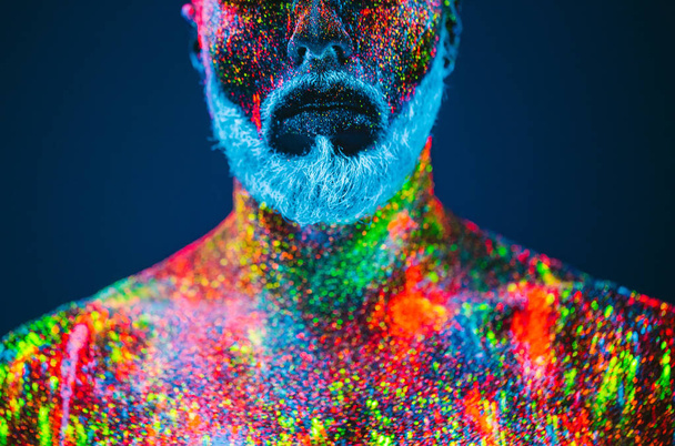 Koncepcja. Portret brodatego mężczyzny. Człowiek jest pomalowany w proszku ultrafioletowe. - Zdjęcie, obraz