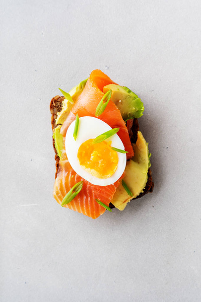Healthy sandwich on multigrain wholegrain toast with avocado, salmon, egg and spring onion on concrete background - Fotó, kép