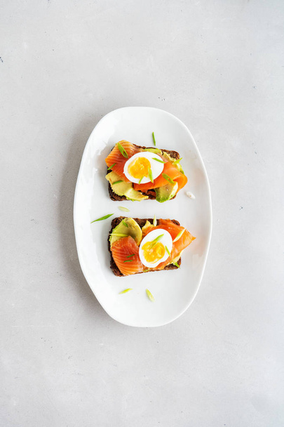 Sandwiches on wholegrain toasts with avocado, salmon, eggs and chopped spring onion on concrete background  - Foto, Imagen