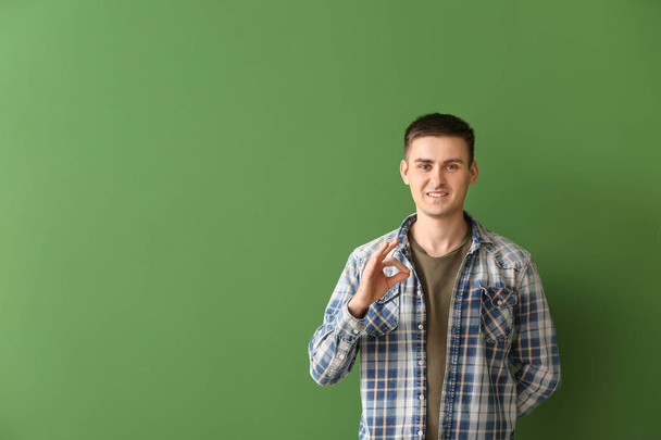 Молодой глухонемой человек использует язык жестов на цветном фоне
 - Фото, изображение