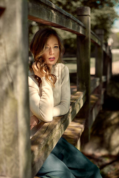 Closeup of an attractive, young woman relaxing at the wooden bridge by the brook.  - Photo, Image