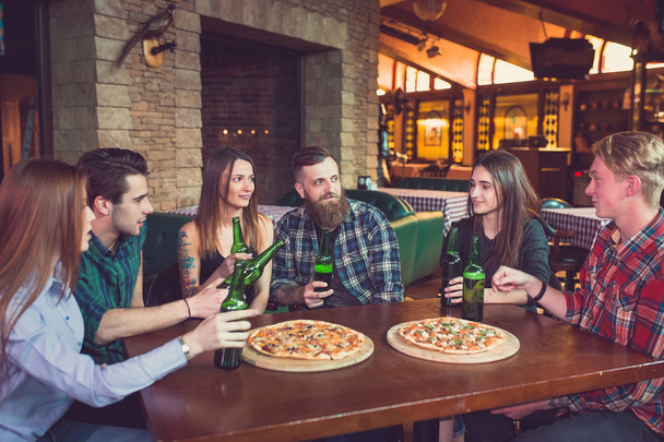 Friends having a drinks in a bar, They are sitting at a wooden table with beers and pizza. - Foto, Bild