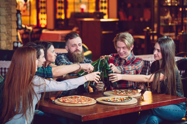 Friends having a drinks in a bar, They are sitting at a wooden table with beers and pizza - Foto, immagini