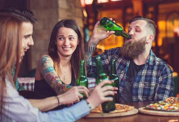 Friends having a drinks in a bar, They are sitting at a wooden table with beers and pizza. - Photo, Image