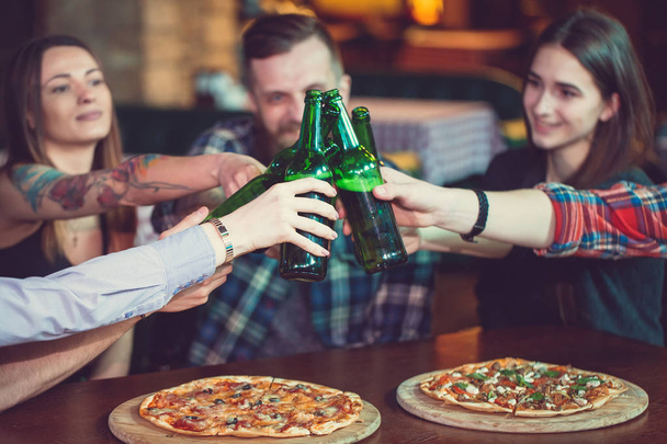 Friends having a drinks in a bar, They are sitting at a wooden table with beers and pizza. - Foto, Bild