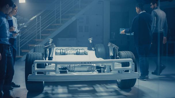 Csapat Automobile design mérnökök autóipari innovációs eszköz dolgozó elektromos autó platform alváz prototípus, amely magában foglalja a kerekek, felfüggesztés, hibrid motor és az akkumulátor - Fotó, kép