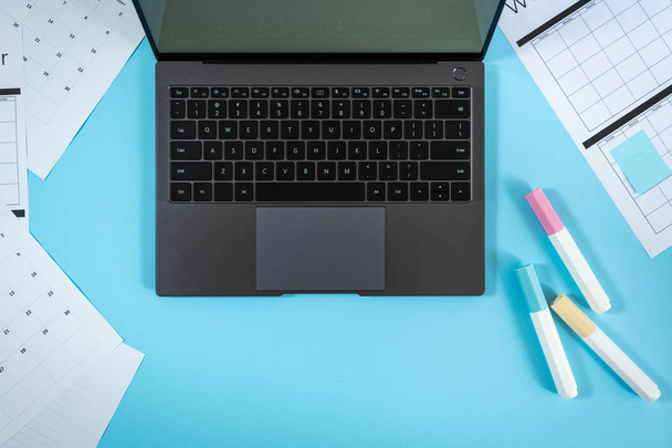 Laptop, επιστολόχαρτα και σχεδιαστής σε μπλε παστέλ φόντο - Φωτογραφία, εικόνα
