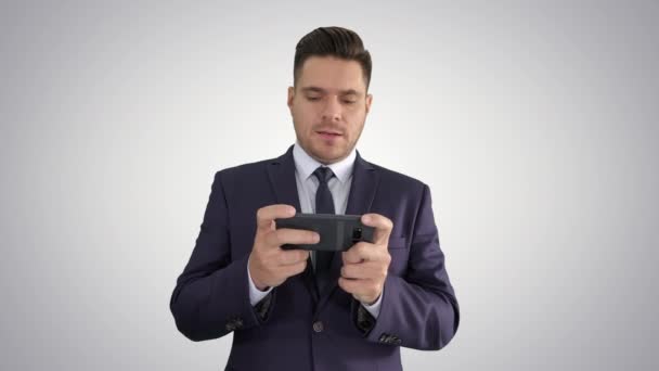 Handsome businessman playing with his smartphone and losing on gradient background. - Video