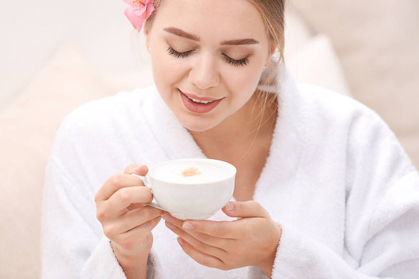Όμορφη νεαρή γυναίκα που πίνει καφέ στο σαλόνι σπα - Φωτογραφία, εικόνα