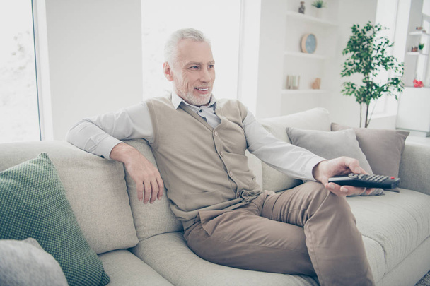 Close up side profile photo amazing funky he him his aged man arms hands console change tv channel media wear specs white shirt waistcoat pants sit comfort bright flat house living room indoors - Foto, Bild