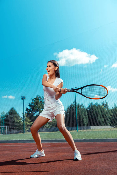 Dark-haired woman screaming while hitting the tennis ball - 写真・画像