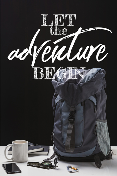 mochila, taza, cuadernos, teléfono inteligente y equipo de trekking aislado en negro con dejar que la aventura comience a escribir
 - Foto, imagen