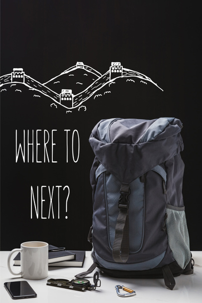 backpack, cup, notebooks, smartphone and trekking equipment isolated on black with where to next question - Photo, Image