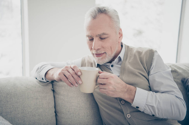 Close up photo amazing he him his aged man overjoyed calm hands arms hot beverage imaginary flight fancy great flavor wear white shirt waistcoat pants sit cozy divan flat house living room indoors - Foto, afbeelding
