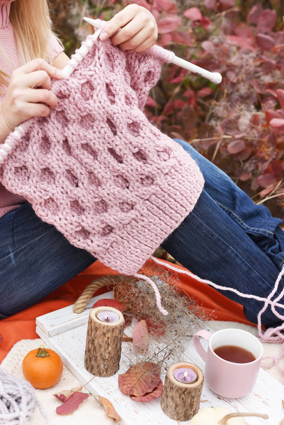 Hands knit needles fluffy pink knitting. The process of knitting in the autumn beautiful garden. - Foto, imagen