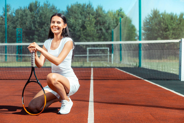 Dark-haired woman wearing sport clothing holding tennis racket - Fotó, kép
