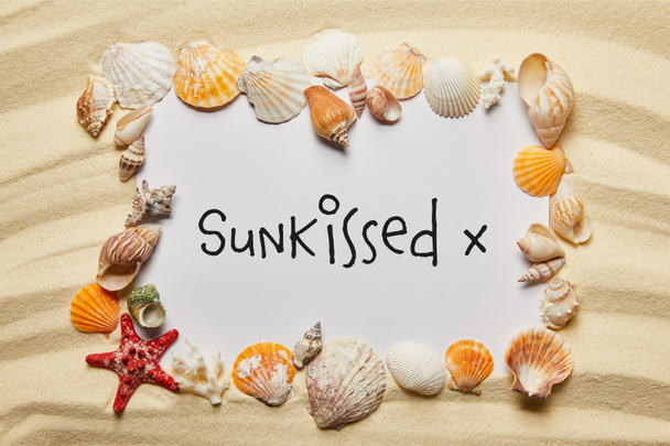 Muschelrahmen neben Plakat mit sonnengeküsstem Schriftzug am Sandstrand - Foto, Bild