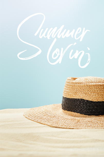 selective focus of straw hat on golden sand in summertime isolated on blue with summer lovin lettering - Photo, Image