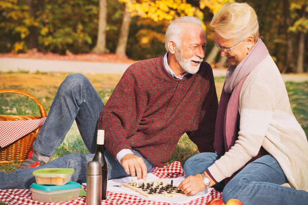 Happy elderly couple sitting on grass and enjoying romantic date - Foto, immagini